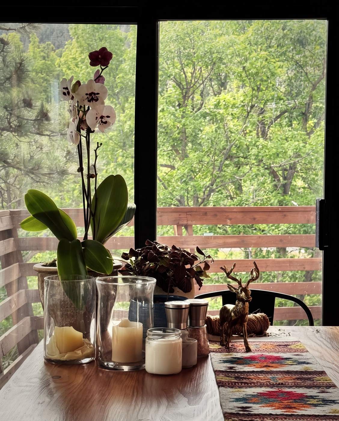 An orchid and candles on the window table, green trees outside